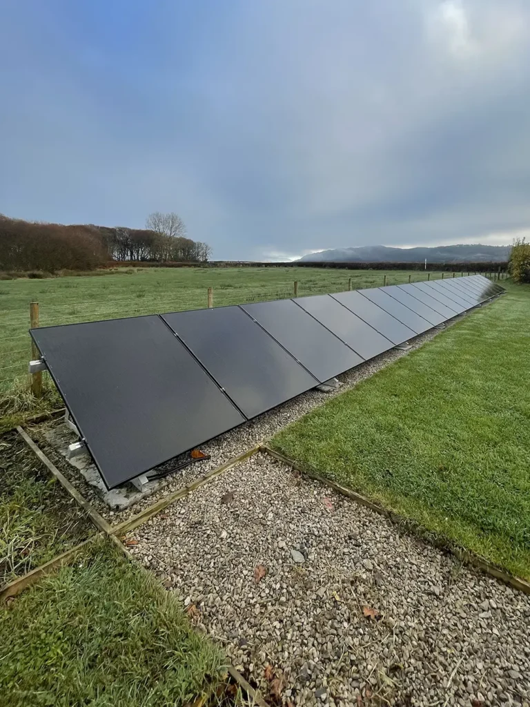 Ground-mounted solar PV system installed in a rural setting, featuring a row of sleek black solar panels on a gravel base, harnessing renewable energy.