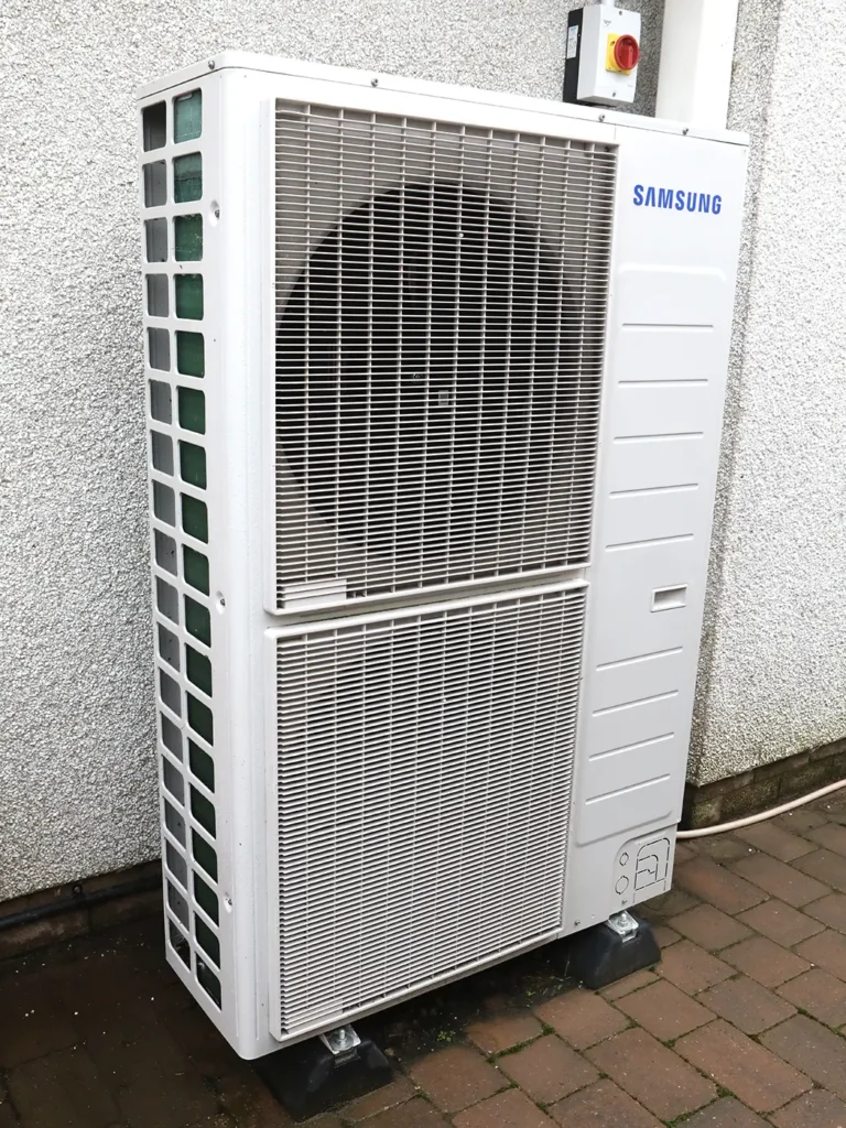 A white Samsung Air Source Heat Pump installed on the side of a residential property.