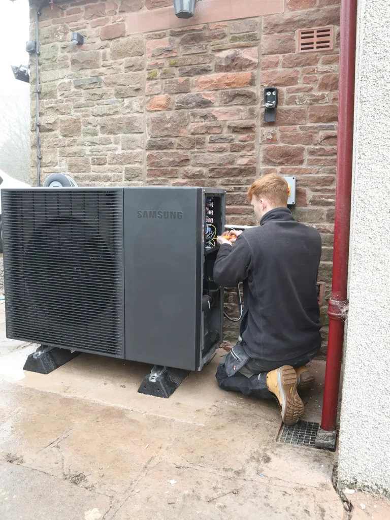 Technician servicing a Samsung air source heat pump installed outside a property with a brick wall.