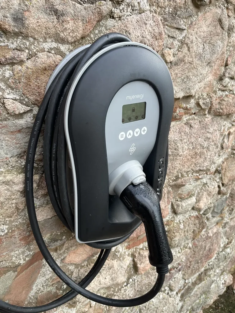 Zappi electric car charger mounted on a stone wall, featuring a coiled charging cable and digital display for efficient EV charging.
